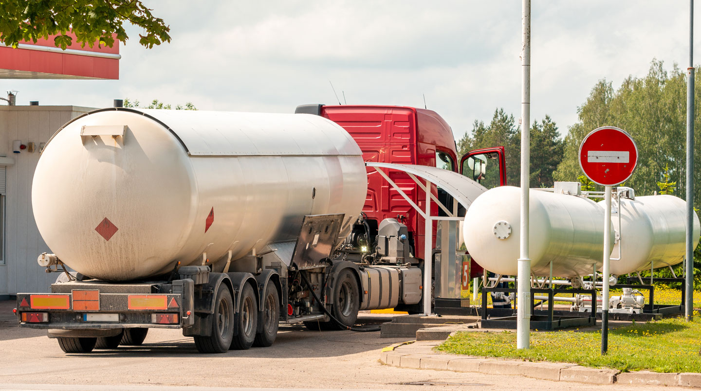 Camion-citerne blanc de livraison de gaz propane en train de remplir une citerne de stockage sur un site professionnel en France, chauffeur-livreur raccordant le flexible de livraison